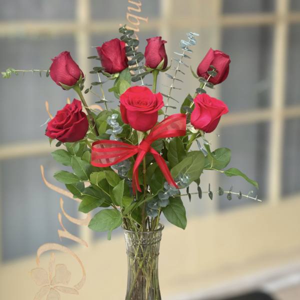 Red roses arranged in a clear glass vase with a red ribbon
