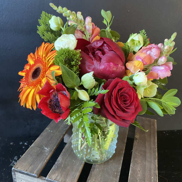 Mixed bouquet in a clear glass vase with red, orange, pink, and white blooms