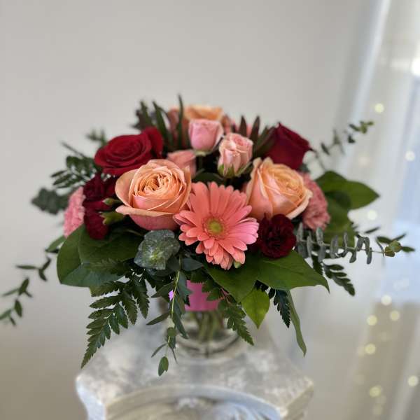 Bouquet of peach and red roses with a pink gerbera daisy in a glass vase