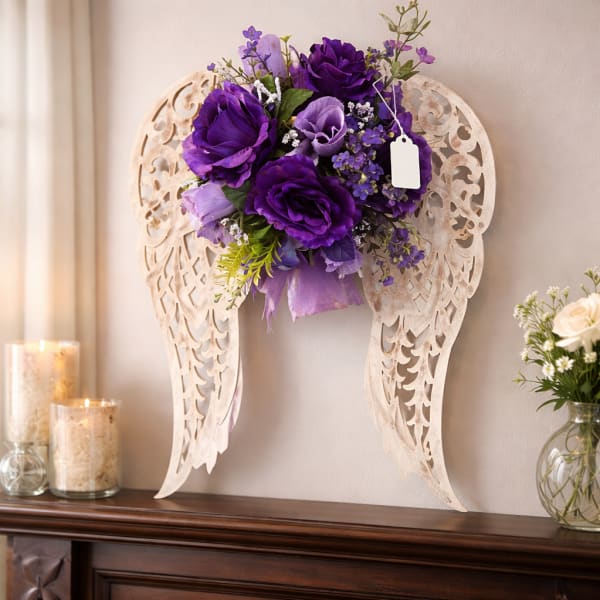 Purple silk flower arrangement on carved angel wing wall decor above a mantel