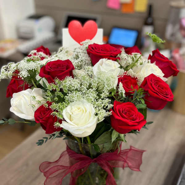 Red and white roses in a glass vase with a red ribbon