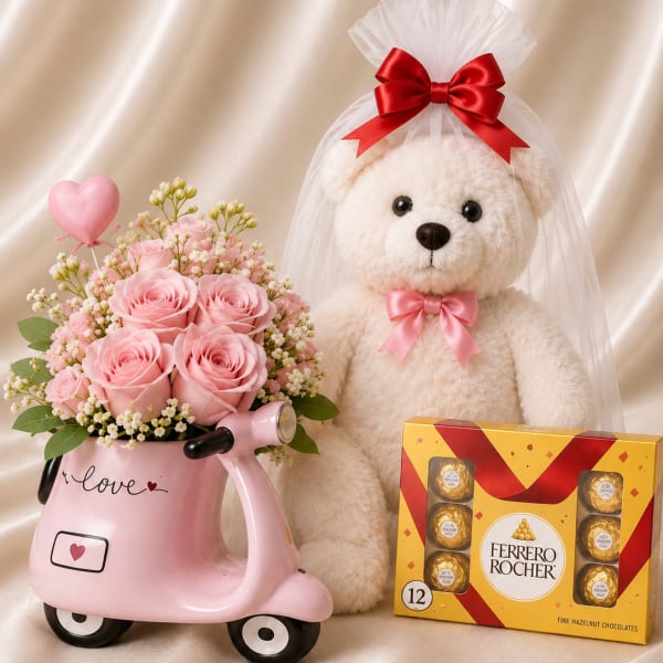 Pink rose bouquet in a scooter-shaped vase beside a teddy bear and chocolates