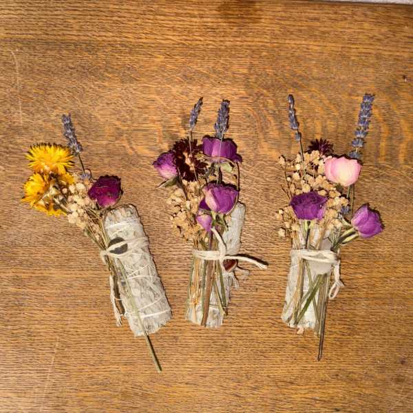 Three small dried flower and sage bundles tied with twine on a wooden surface