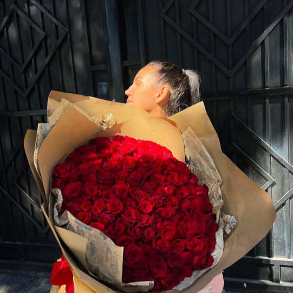 Woman holding a large bouquet of red roses wrapped in brown paper