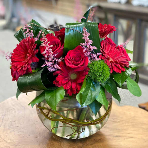 Red roses and gerbera daisies in a glass bowl vase