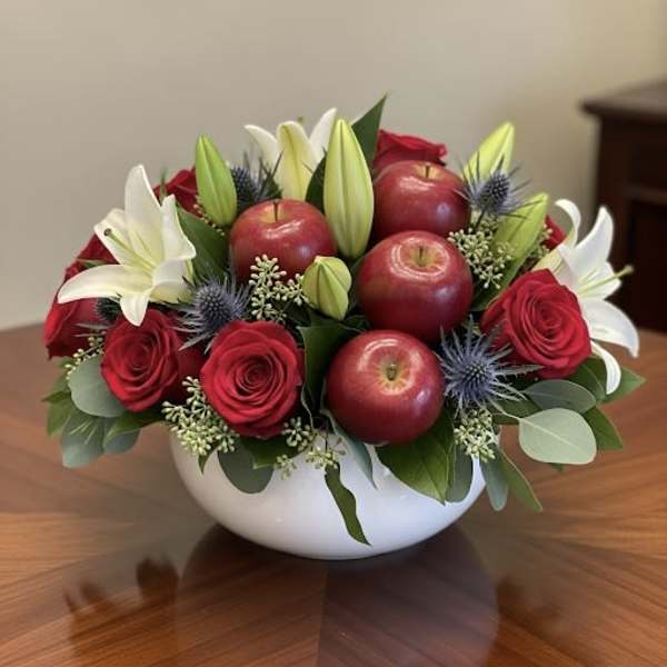 Red roses and white lilies arranged with apples in a white bowl.