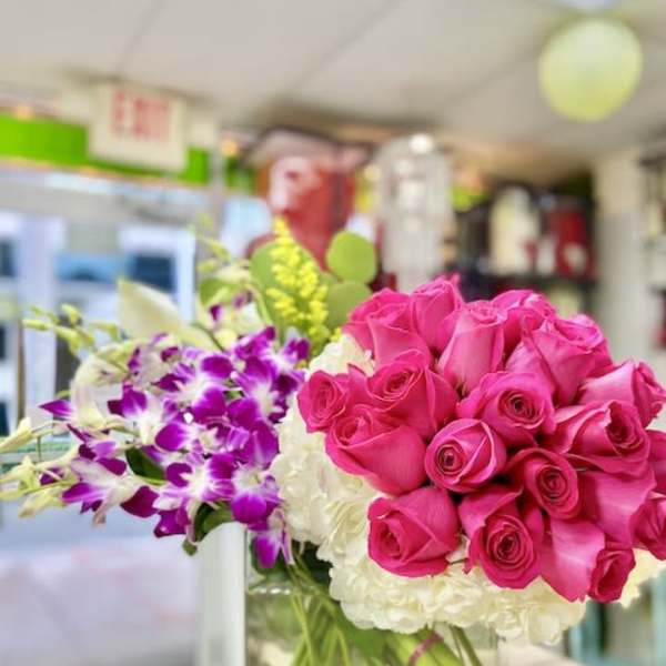 Square vase arrangement with hot pink roses, white hydrangeas, and purple orchids on a wooden surface