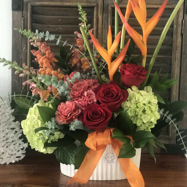 Tropical floral arrangement with red roses, hydrangeas, and orange bird-of-paradise in a white container
