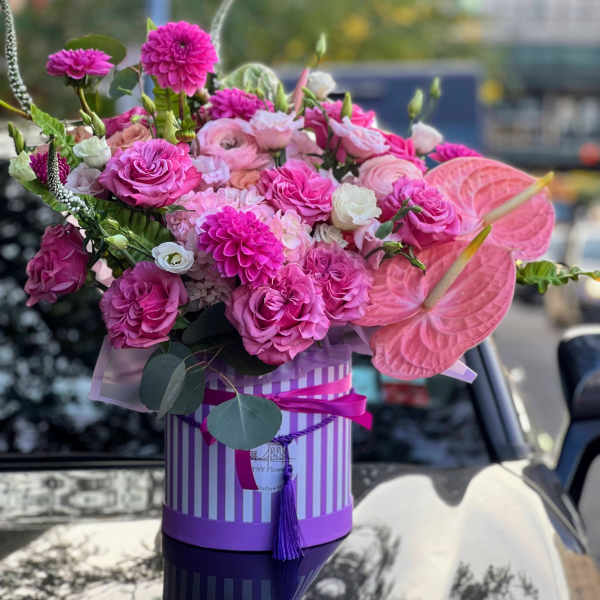 Pink floral arrangement in a striped hatbox with anthuriums and roses
