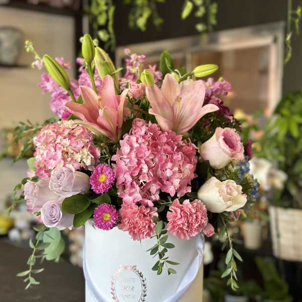 Pink lilies, hydrangeas, roses, and carnations arranged in a round white hatbox.