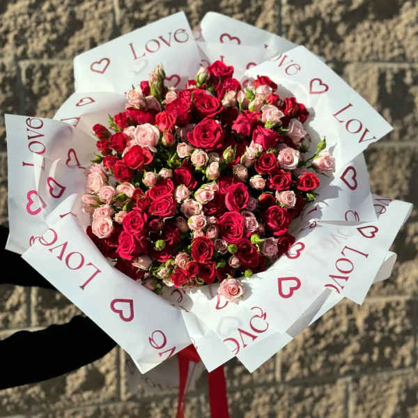 Bouquet of red and pink roses wrapped in white paper with heart prints