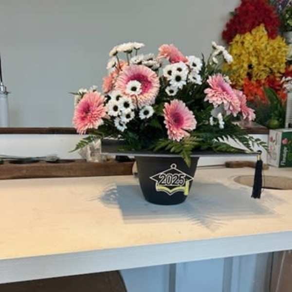 Pink and white flowers arranged in a black graduation cap container
