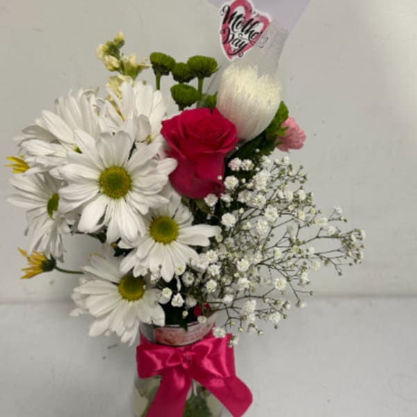 Bouquet of white daisies and a pink rose in a glass vase with a pink ribbon
