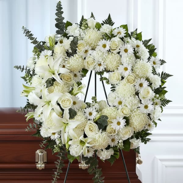 White floral wreath on a stand displayed over a casket