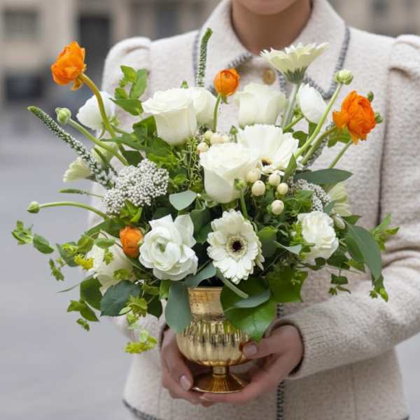White and orange floral arrangement in a gold vase