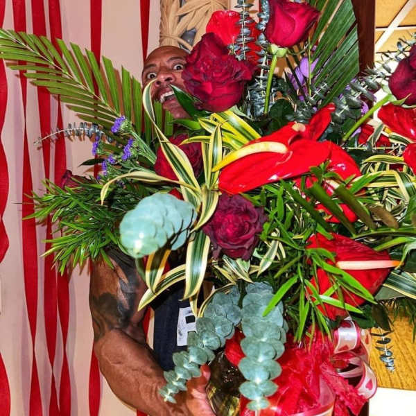 Large bouquet of red roses and tropical foliage held by a man