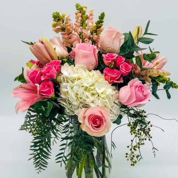 Pink roses and lilies arranged in a glass vase with white hydrangea