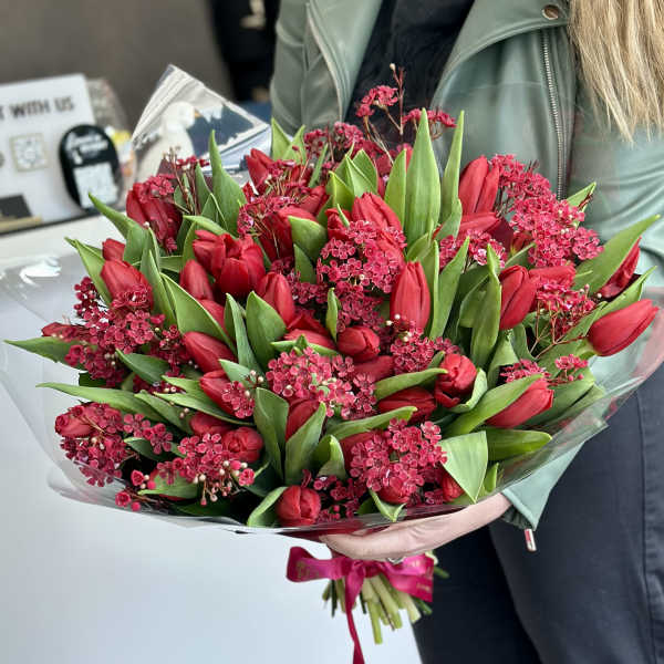 Bouquet of red tulips and pink filler flowers wrapped in clear plastic