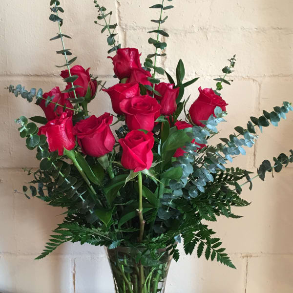 Red roses in a clear glass vase with tall eucalyptus stems