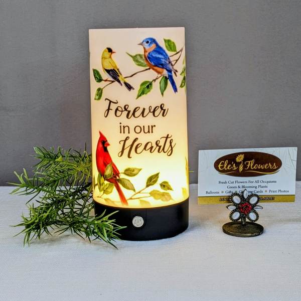 Lit memorial candle with birds and the words Forever in our Hearts