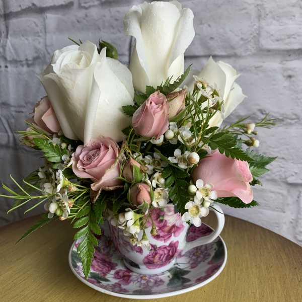 White and pink roses arranged in a floral teacup with saucer