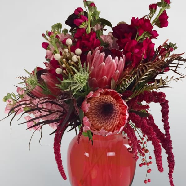 Pink and burgundy floral arrangement in a red glass vase