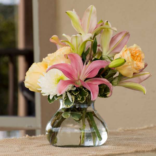 Pink lilies and pale roses arranged in a clear glass vase