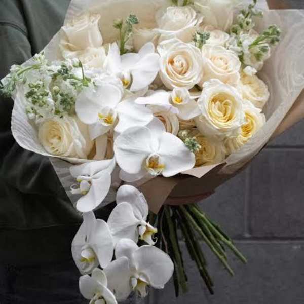 White roses and orchids in a hand-tied bouquet with cream wrapping