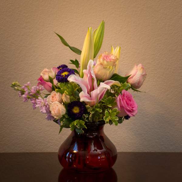 Mixed bouquet of lilies, roses, and purple daisies in a red glass vase