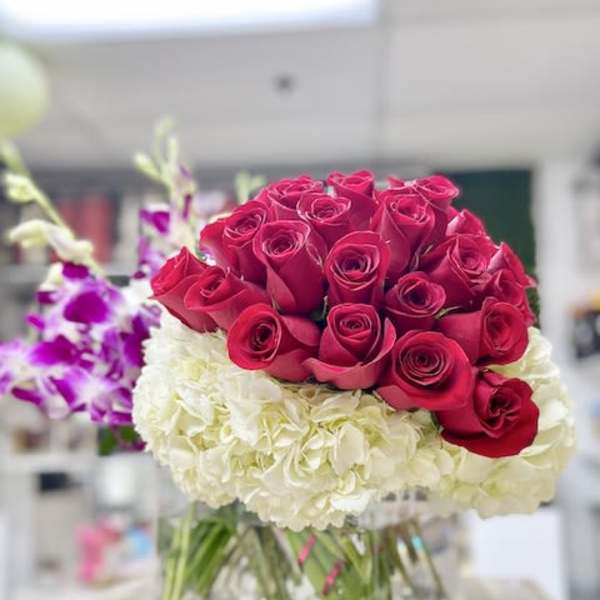 Red roses arranged over white hydrangeas with purple orchids in a clear square glass vase