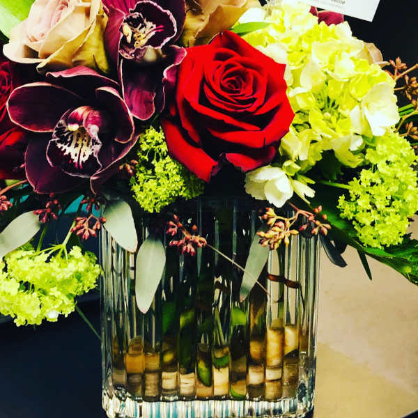 Bouquet of red roses, orchids, and pale hydrangeas in a glass vase
