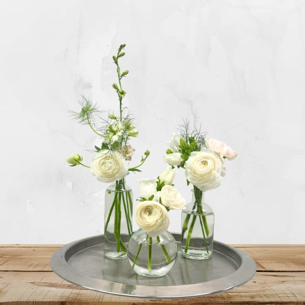Three small white floral arrangements in clear glass vases on a metal tray