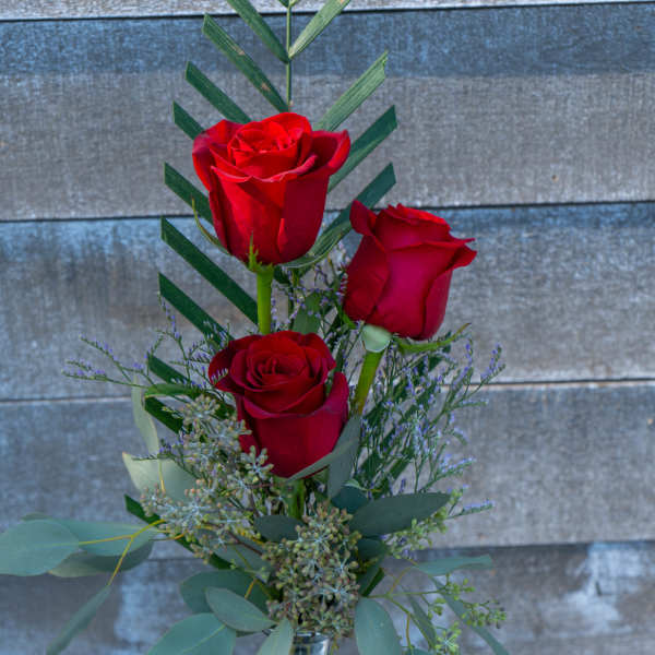 Three red roses in a clear glass vase with greenery