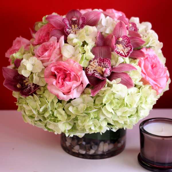 Low round bouquet of pink roses, green hydrangeas, and pink orchids in a glass vase