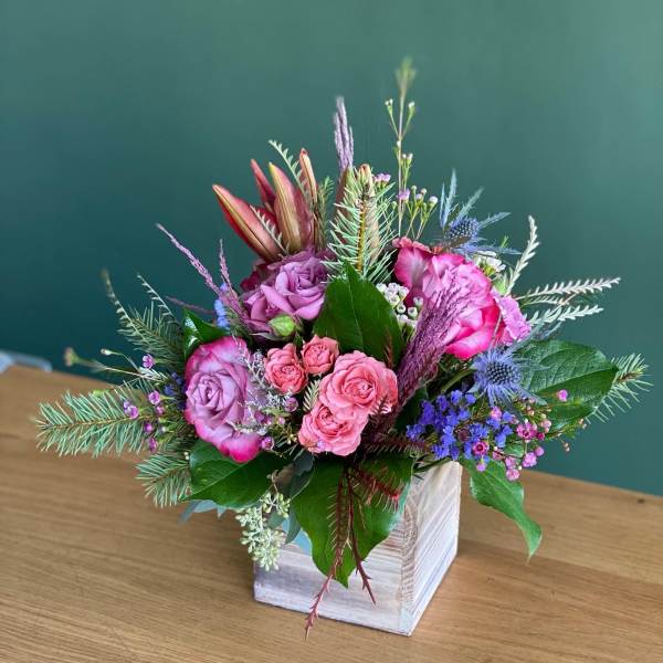 Pink and purple flower arrangement in a white wooden box