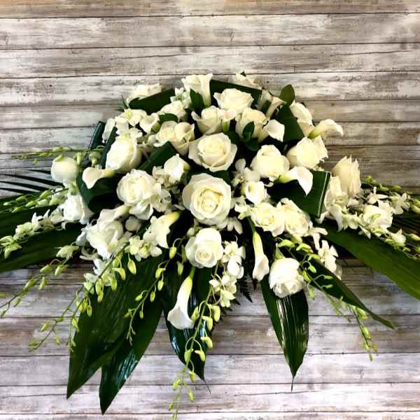 White roses and calla lilies arranged with orchids and broad leaves