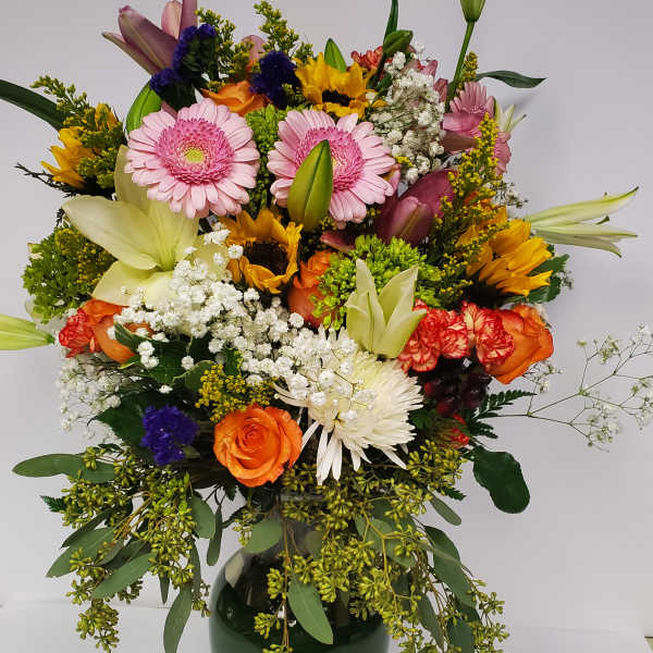 Mixed bouquet of pink gerbera daisies, sunflowers, roses, and lilies in a vase