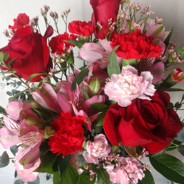 Bouquet of red roses, pink alstroemeria, and carnations in a glass vase
