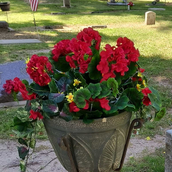 Red flowers arranged in a cemetery planter on a metal stand
