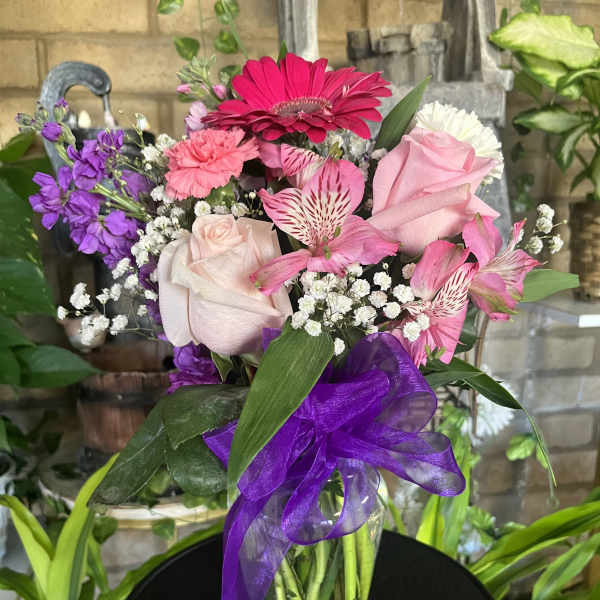 Pink and purple mixed bouquet in a glass vase with a purple ribbon