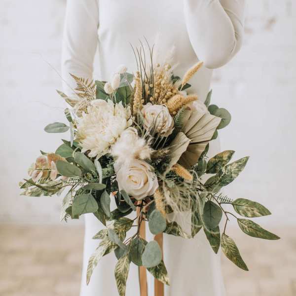 Bride holding a cream and green bouquet with roses and dried grasses