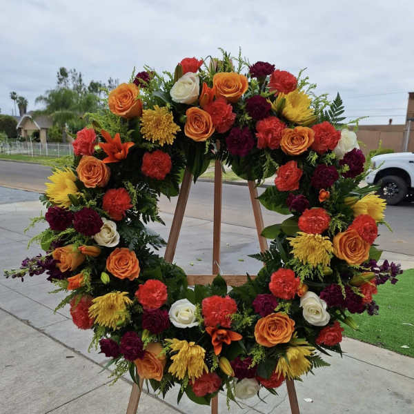 Large floral wreath on a wooden stand with orange, red, yellow, and white blooms