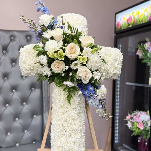White floral cross arrangement with cream roses and blue accents on an easel