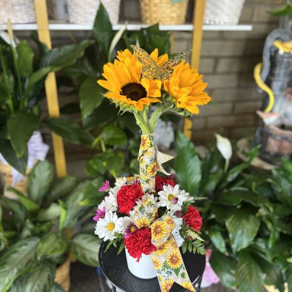 Sunflowers and mixed daisies in a white container with a decorative ribbon