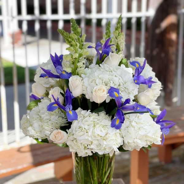 White hydrangea and roses with purple irises in a glass vase
