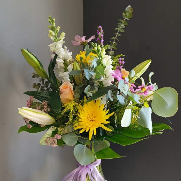 Mixed bouquet with yellow chrysanthemum, lilies, roses, and a lavender ribbon in a glass vase
