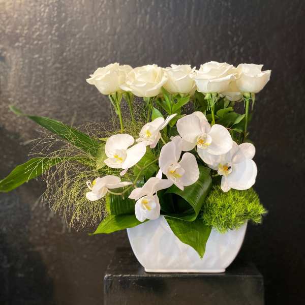 Modern white arrangement of roses and orchids in a white vase with bold green accents.