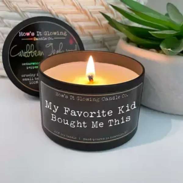 Lit candle in a black tin with a plant in the background