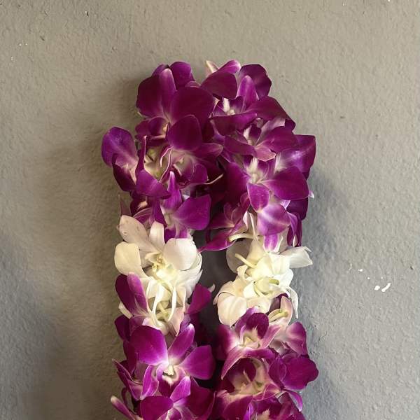 Purple and white orchid lei hanging against a gray wall