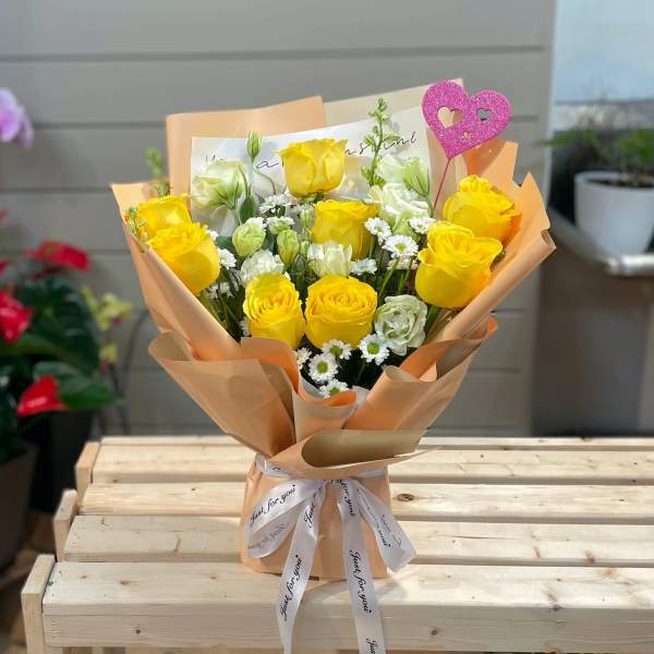 Yellow roses and white flowers in peach wrapping with a pink heart topper